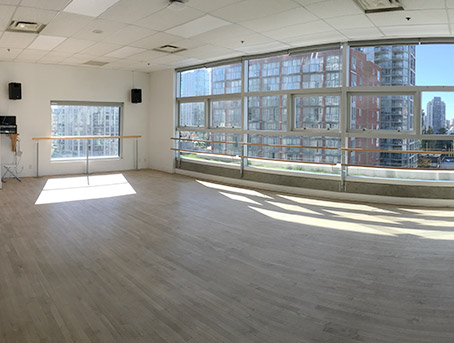 An empty dance studio with bars against the windows with sun streaming through the windows