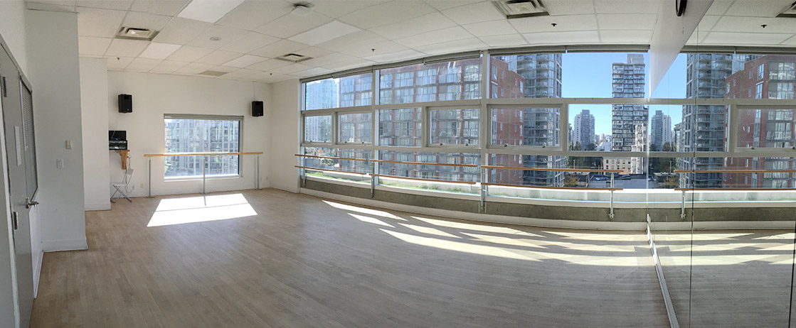 An empty dance studio with bars against the windows with sun streaming through the windows