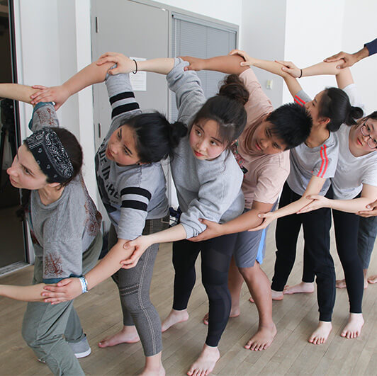 Group of young people in a dance studio stand in a line with their arms linked