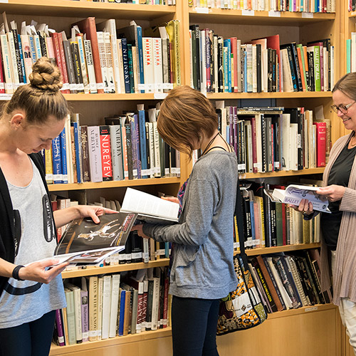 Three women stand in library reading