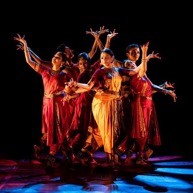 Rama Vaidyanathan and ensemble dancers pose together with their arms extended and bent on a stage