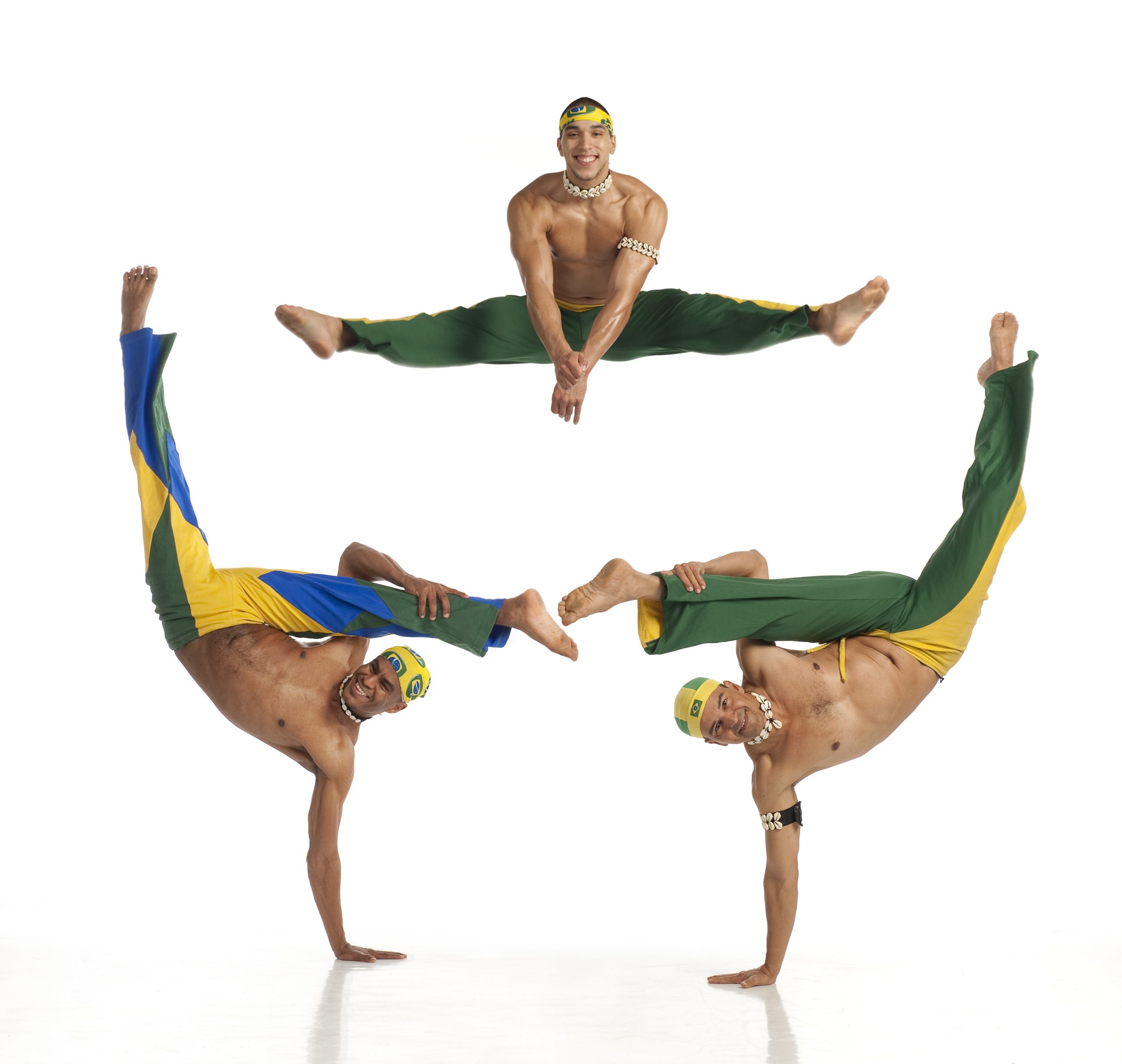 Three Brazillian dance artists. Two are balancing on one arm with their legs up above them. Above them is another dance artist jumping with their legs extended. They are all wearing pants with the colours of the Brazillian flags.